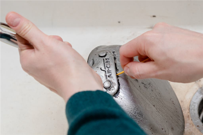 Человек использует зубочистку для удаления налета на ручке кастрюли из нержавеющей стали.